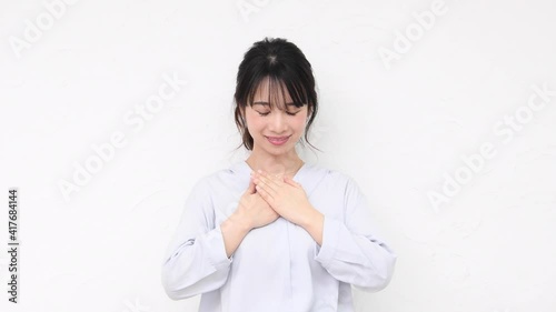 白い壁の前に立って胸に手を当てる若い女性