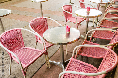 Pink plastic wicker chairs and round silver tables with pink cups containing sugar outside a bistro. 