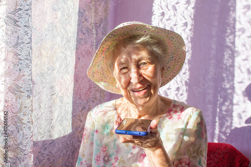 Charming elderly woman in rectangular black rimmed eyewear using voice recognition function on cell phone. © Solarisys
