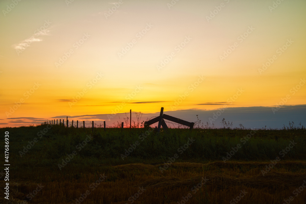 A beautiful orange sunset over a fenced pasture with cut hay in a countryside summer landscape A beautiful orange sunset over a fenced pasture with cut hay in a countryside summer landscape