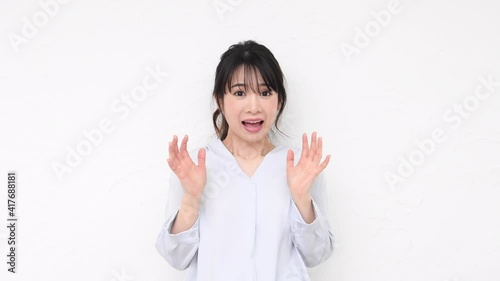 白い壁の前で驚いたジェスチャーをする若い女性