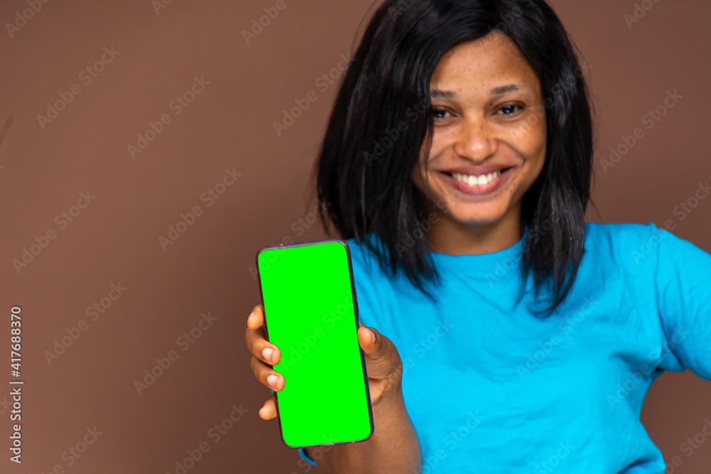 smiling young african lady, holding her phone and showing the blank green screen, focus on phone smiling young african lady, holding her phone and showing the blank green screen, focus on phone