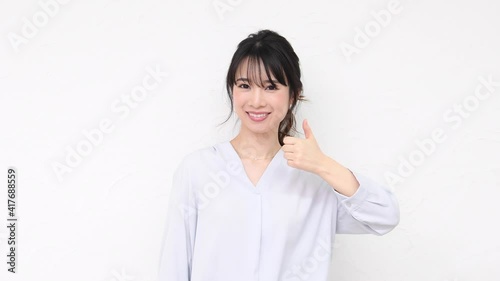 白い壁の前に立って、いいねのジェスチャーをする若い女性