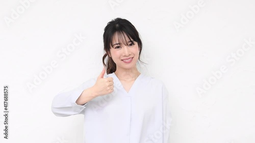 白い壁の前に立って、いいねのジェスチャーをする若い女性
