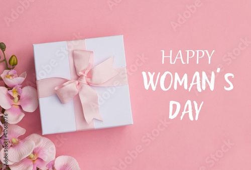 Happy Women's Day text , pink orchids and a gift box on pink background. Happy Women's Day text on pink background.