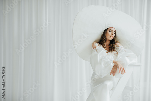 Fashion studio photo of elegant lady in giant white hat. Health and beauty