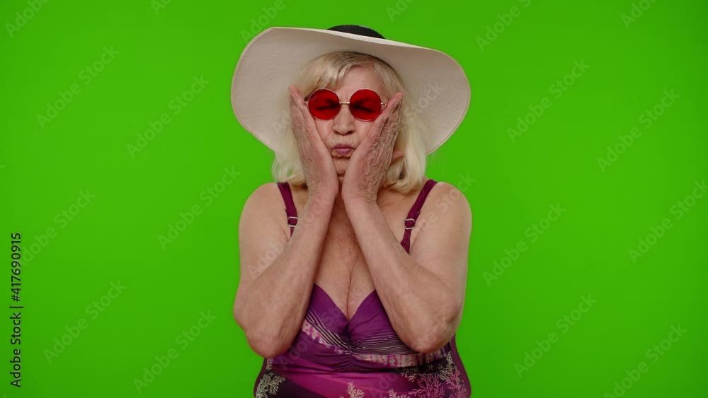 Funny silly senior pensioner woman tourist in swimsuit, fooling around making stupid face brainless dumb expressions on chroma key background. Portrait of old granny traveler model on summer vacations
