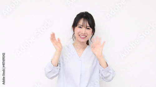 白い壁の前に立って手を振る若い女性
