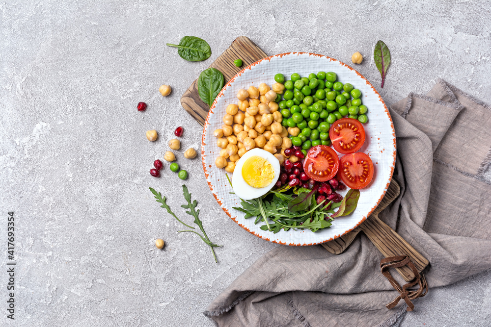 A plate of healthy food: chickpeas with mix of fresh leaves, pomegranate, green peas, cherry tomatoes and boiled egg