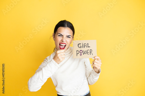Young beautiful activist woman protesting holding poster with girl power message Punching fist to fight, aggressive and angry attack, threat and violence