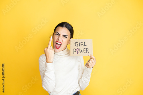 Young beautiful activist woman protesting holding poster with girl power message showing middle finger doing fuck you bad expression, provocation and rude attitude. screaming excited