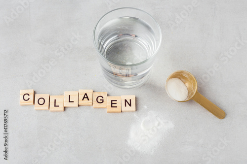 collagen powder with a glass of water on a gray background, spoon, letters