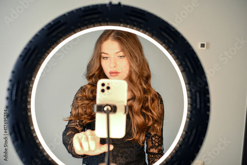 Girl having fun creating videos using beauty skincare mask - Young woman streaming online using smartphone and led soft box - technology, digital job concept - Focus on her face. LED Ring.