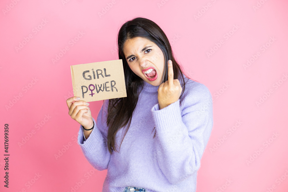 Young beautiful activist woman protesting holding poster with girl power message showing middle finger doing fuck you bad expression, provocation and rude attitude. screaming excited Young beautiful activist woman protesting holding poster with girl power message showing middle finger doing fuck you bad expression, provocation and rude attitude. screaming excited