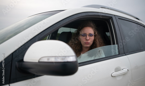 Sad and overwhelmed woman inside her white car while waiting in a traffic jam. © Clipfy