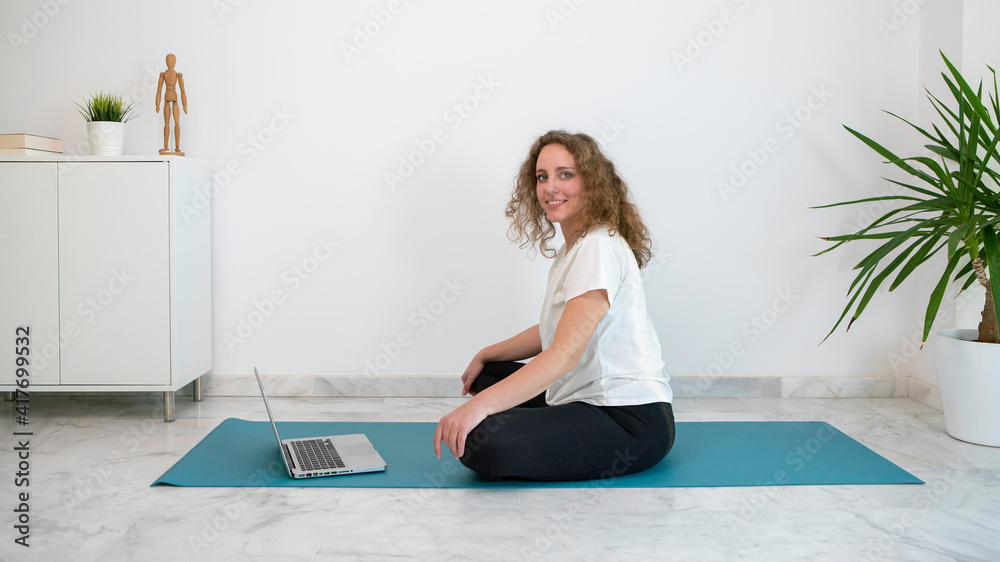 Woman with curly blond hair practicing a yoga class with her computer from home. Woman with curly blond hair practicing a yoga class with her computer from home.