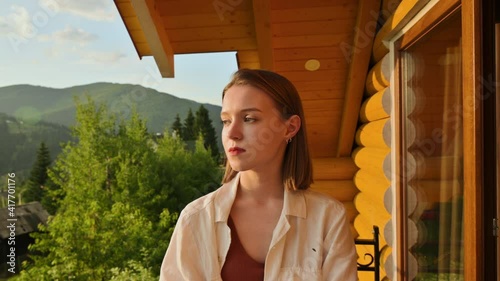 Close portrait of attractive woman on apartment balcony against mountains background, llooks at the camera and to the side at the beautiful landscape photo