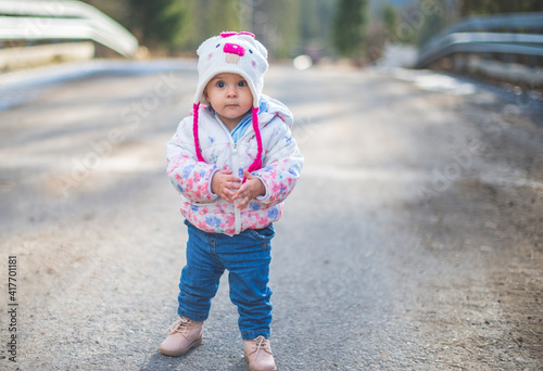 Portrait of little toddler girl walking and having fun outdoors in cold weather at mountains