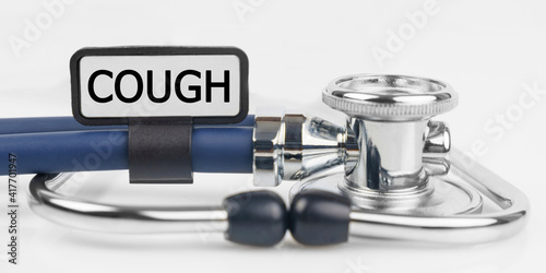 On the white surface lies a stethoscope with a plate with the inscription - COUGH