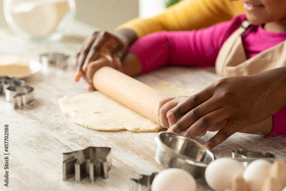 Black mom and daughter rolling up dough for cookies in kitchen together