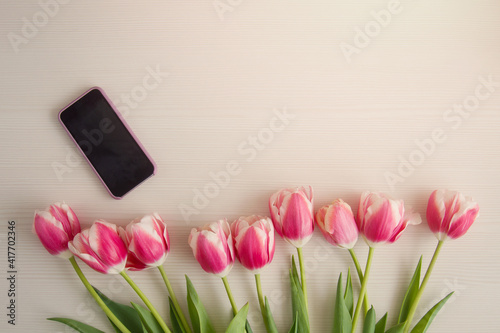 Pink and white tulips and mobile phone for mockup on a wooden background with place for text. Horizontal format, top view. Copyspace
