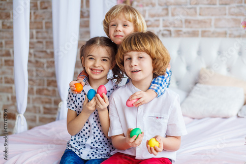 Easter children portrait, funny emotions, surprise. Children, a girl and two boys hold Easter eggs in their hands. Funny photo. Adorable kid in colored clothes enjoying holiday