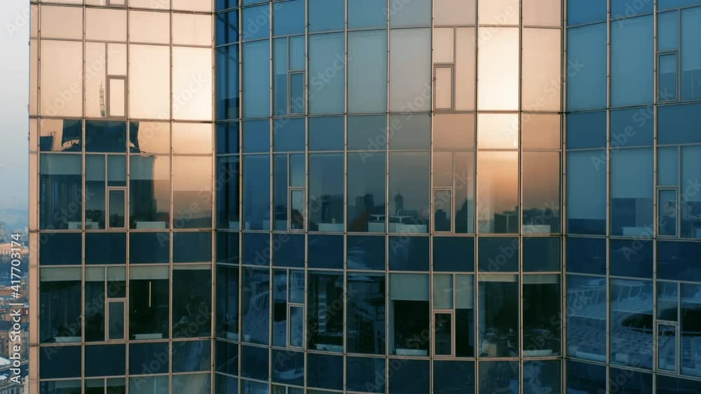 Aerial elevator shot of a modern glassed office skyscraper exterior with cityscape reflection in the windows at sunset or dawn