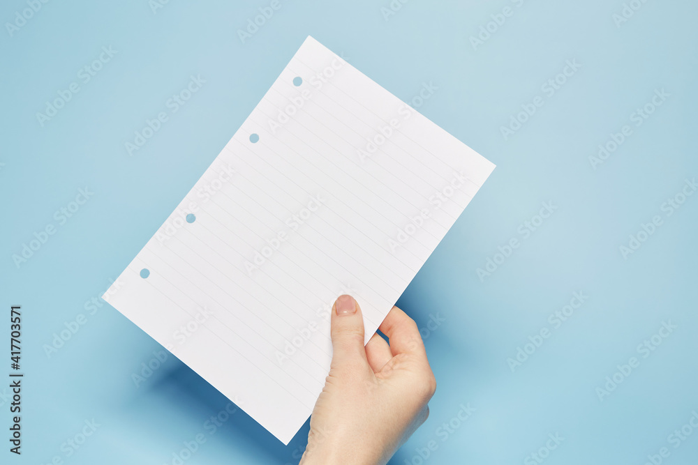 Template for text message: Hand holding the notebook bland lined paper sheet with the copy text space on the bright solid blue fond background Template for text message: Hand holding the notebook bland lined paper sheet with the copy text space on the bright solid blue fond background