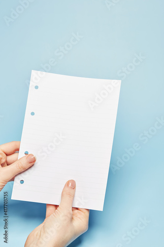 Template for text message: Hand holding the notebook bland lined paper sheet with the copy text space on the bright solid blue fond background
