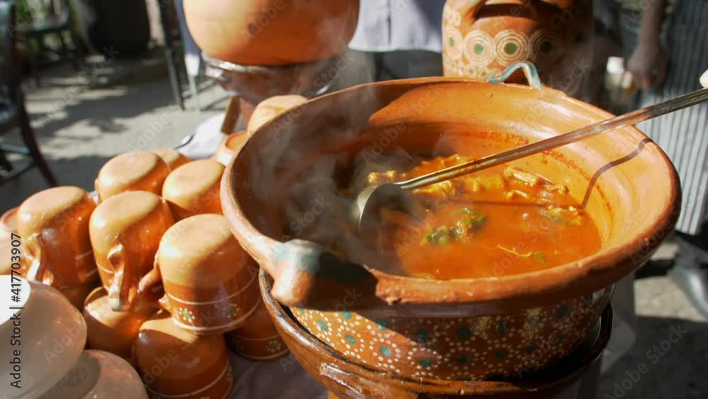 Spoon stirring tasty-looking Mexican beef stew in clay pot