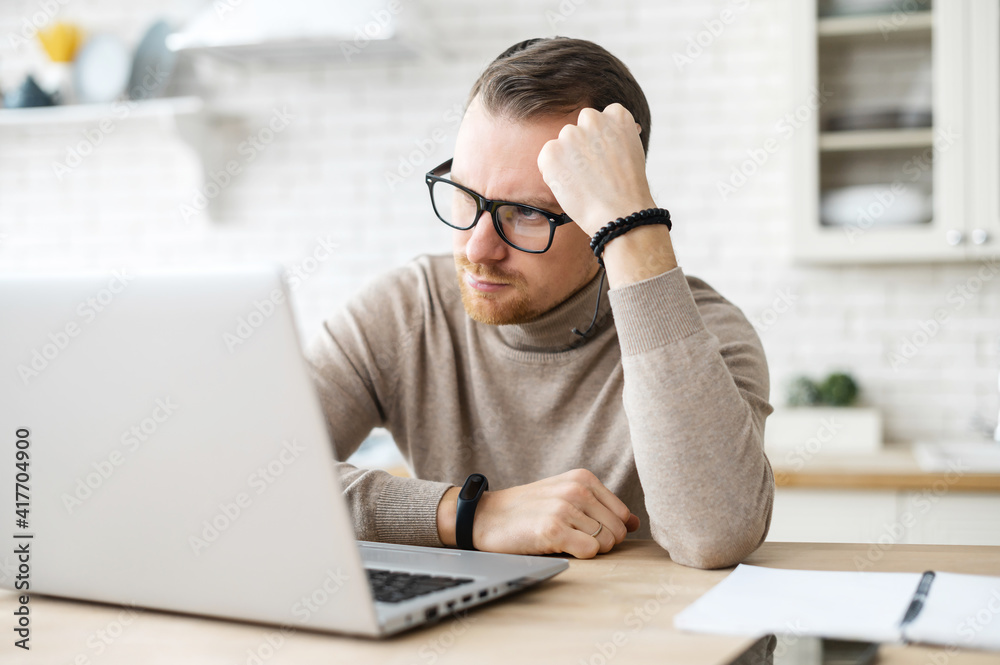 Business man sit at table in kitchen near laptop, resting head on his hand, thinks over strategy, work remotely from home, creative job, generating new fresh ideas, searching solution. Doubts concept