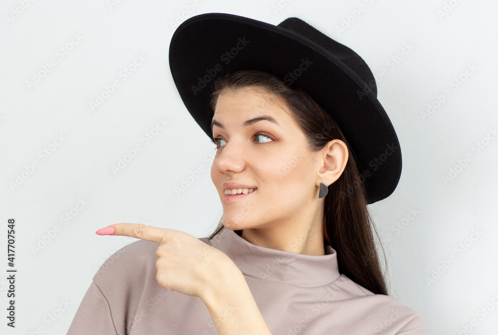 Happy surprised young female smiling broadly at camera, pointing fingers away, showing something interesting and exciting on studio wall with copy space for your text or advertising content Happy surprised young female smiling broadly at camera, pointing fingers away, showing something interesting and exciting on studio wall with copy space for your text or advertising content
