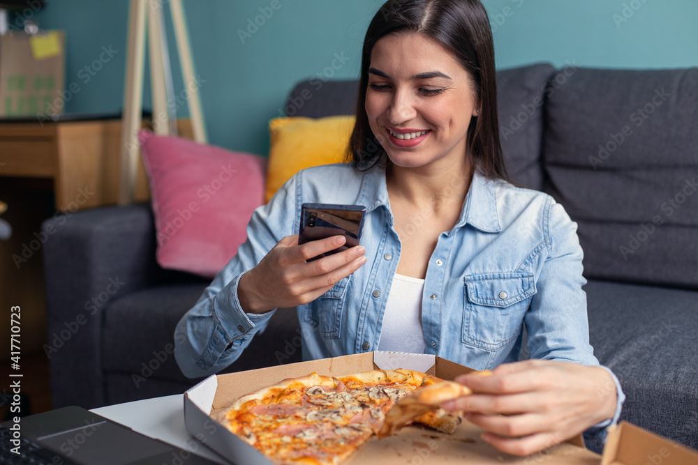 A young woman is eating pizza taking a selfie.