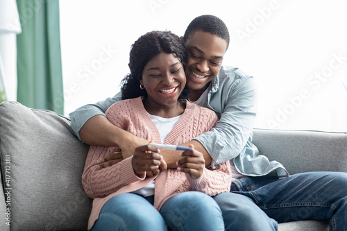 Happy pregnant black couple with pregnancy test at home