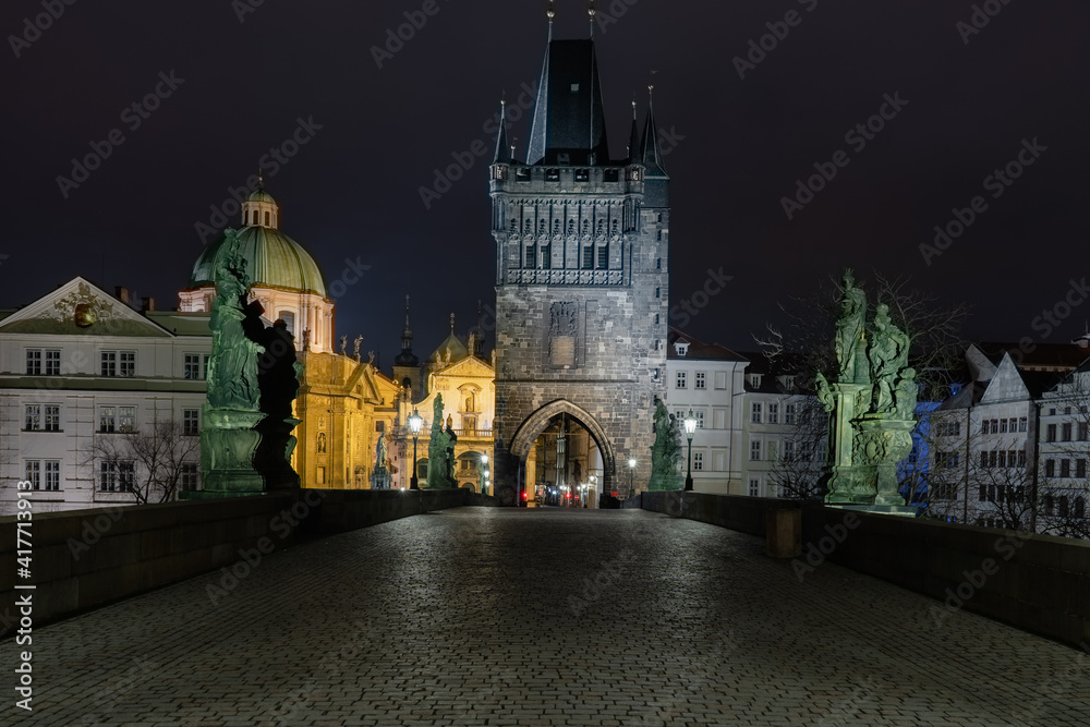 view of the bridge tower and cobblestone walkway on Charles Bridge and lighted lanterns at night in the center of Prague