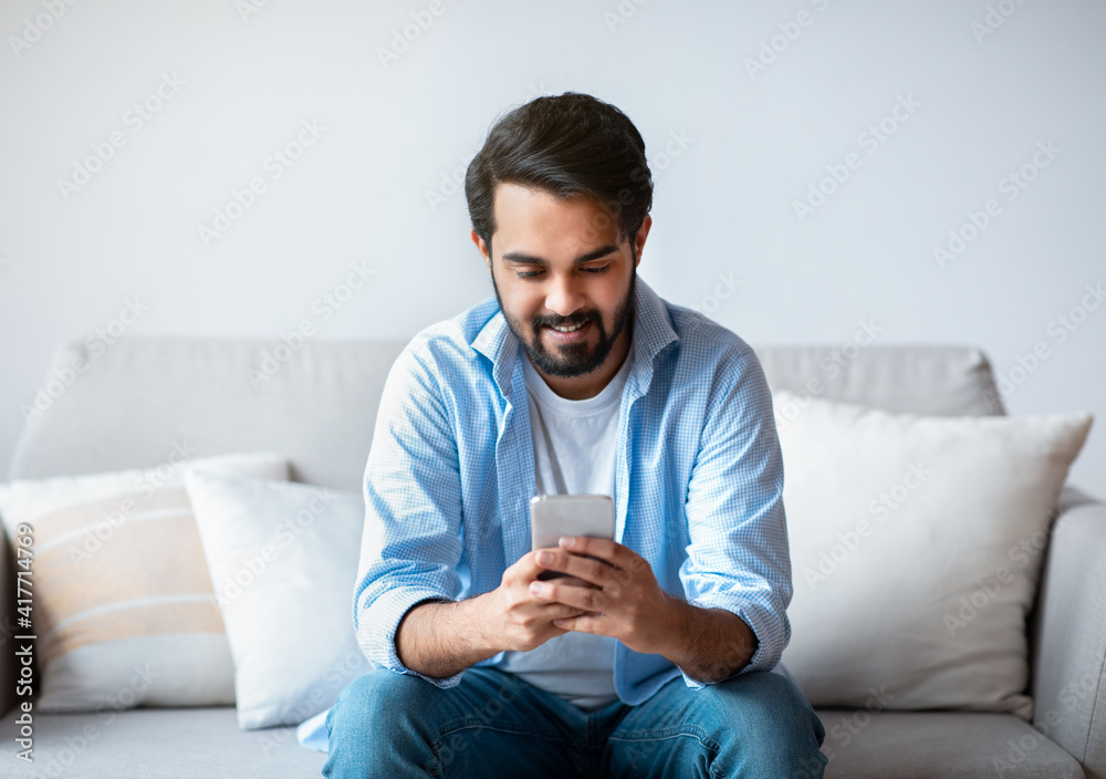 Happy arab man using smartphone at home, messaging with friends Happy arab man using smartphone at home, messaging with friends