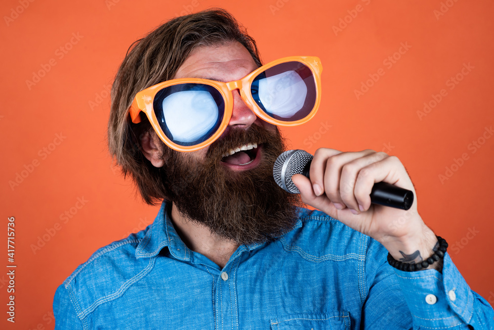 nice voice. karaoke and music. male speaker with mic. vocal. happy smiling mature man. guy with beard sing in microphone. brutal caucasian hipster event manager. funny party glasses