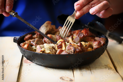 Soft focus. Frying pan with fried meat. The man is eating fried meat pieces.