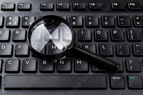 Magnifying glass on the black computer keyboard closeup. Find keywords and online resources, network search, Internet security concepts. Detection of computer viruses.