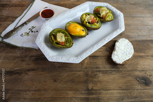 baked avocado stuffed with egg, vegetables, lie on a white dish, bread smeared with curd mass, linen napkin with embroidery, concept of post-holiday detox, diet, healthy food