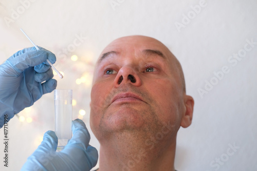 face of an elderly bald man close-up, laboratory assistant, doctor takes swab sample from the nasal mucosa for test for coronavirus, DNA determination, concept of COVID-19