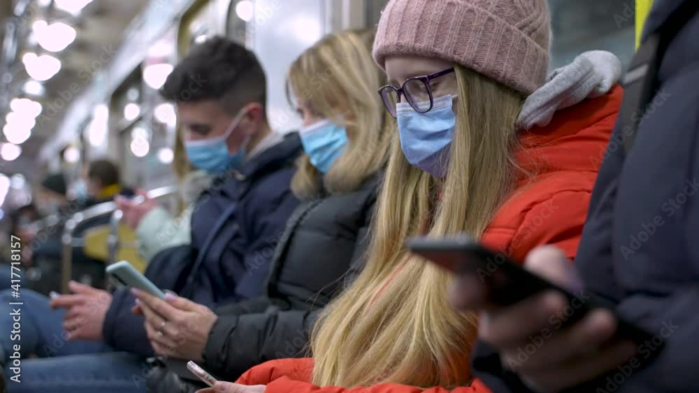 Focused subway passengers wearing medical face masks and winter jackets using cellphones while riding in metro car during coronavirus pandemic. Masked people during ride in underground carriage