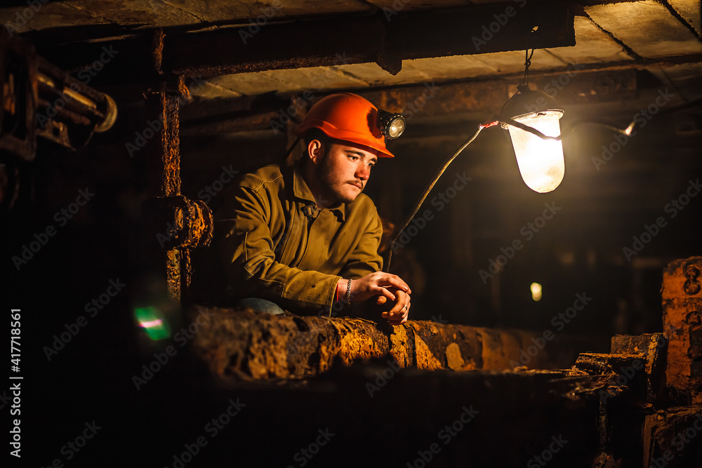 Obraz premium A tired miner in a coal mine looks at the light. Work in a coal mine. Portrait of a miner. Copy space.