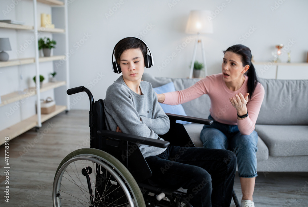 Depression in disabled teens. Sad adolescent in wheelchair shutting himself off from world, mother trying to talk to him Depression in disabled teens. Sad adolescent in wheelchair shutting himself off from world, mother trying to talk to him