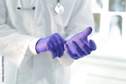 Doctor with stethoscope in a medical gown puts on protective gloves in a hospital