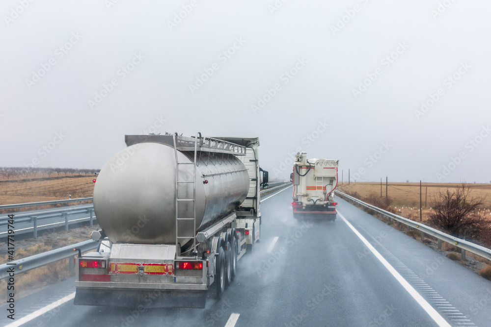 Tank truck overtaking an animal feed truck on a rainy day.