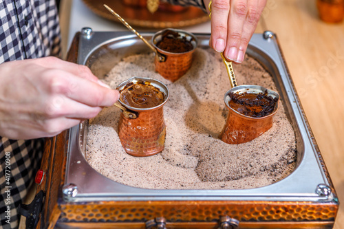 The barista brews natural coffee in copper turks on the sand. The process of making a drink.