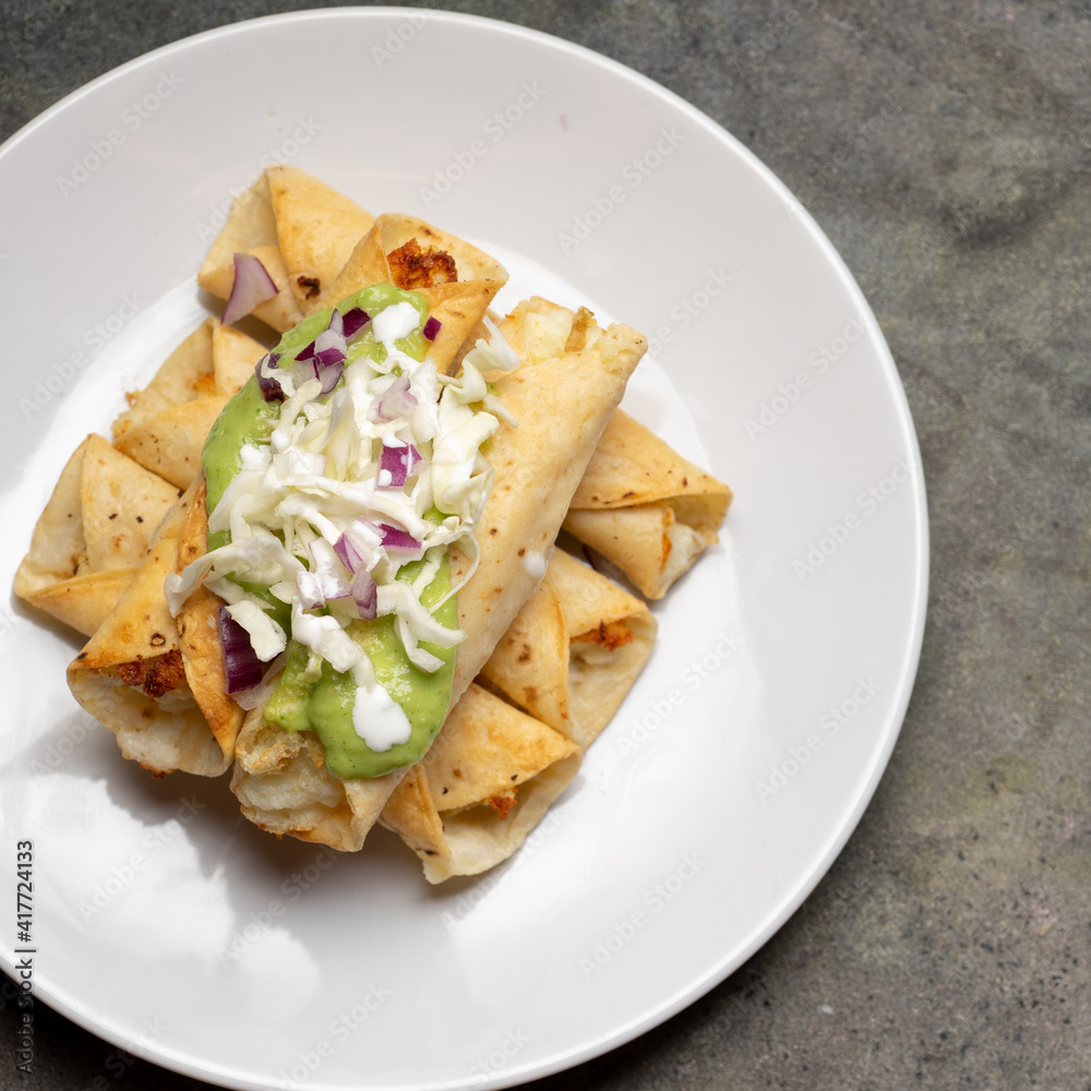 Fried tacos called flautas with guacamole and cabbage on dark background. Mexican food Fried tacos called flautas with guacamole and cabbage on dark background. Mexican food