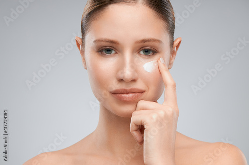 Attractive smiling young lady putting cream on her face. Beauty photography