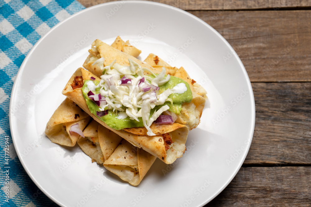 Fried tacos called flautas with guacamole and cabbage on wooden background. Mexican food Fried tacos called flautas with guacamole and cabbage on wooden background. Mexican food